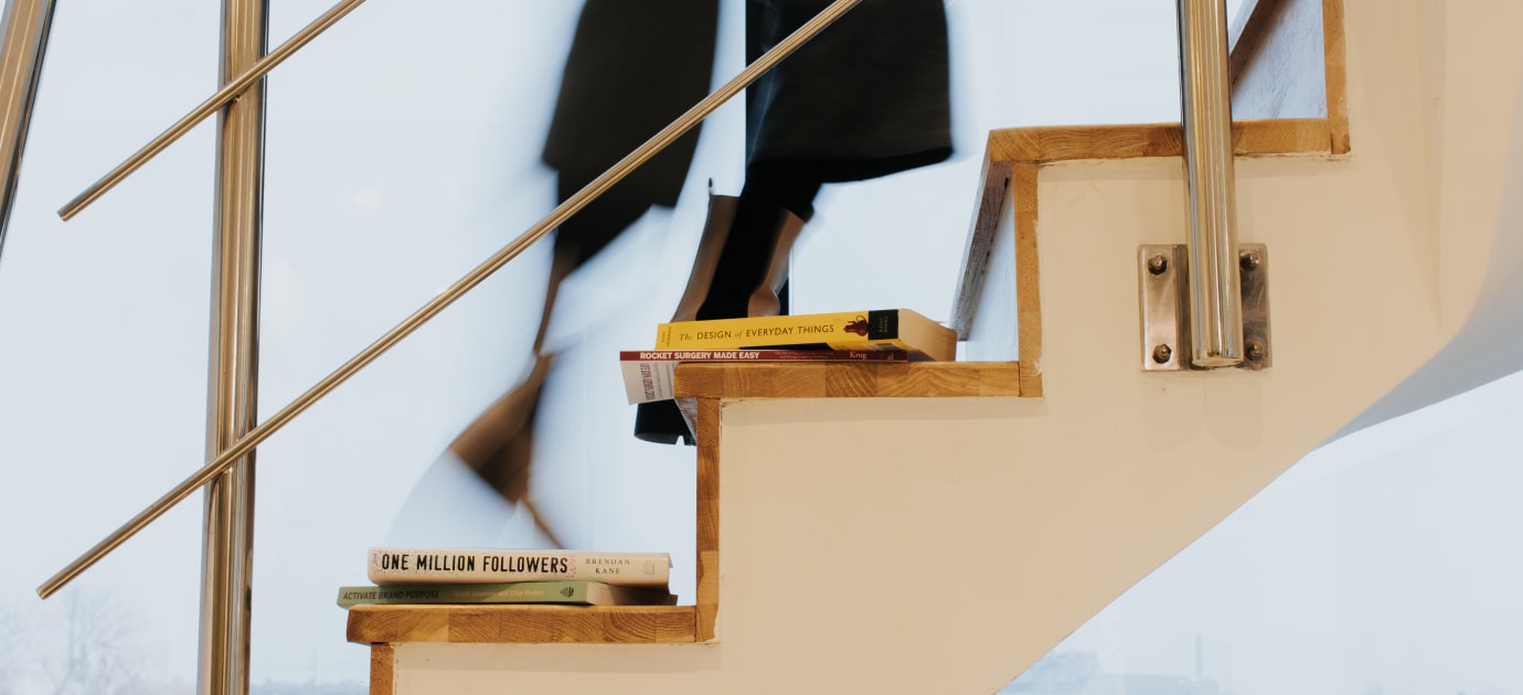 A woman climbing stairs with 4 books on steps, her legs visible in motion.